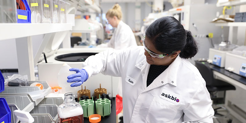 An AskBio lab professional pouring a liquid solution into a container.