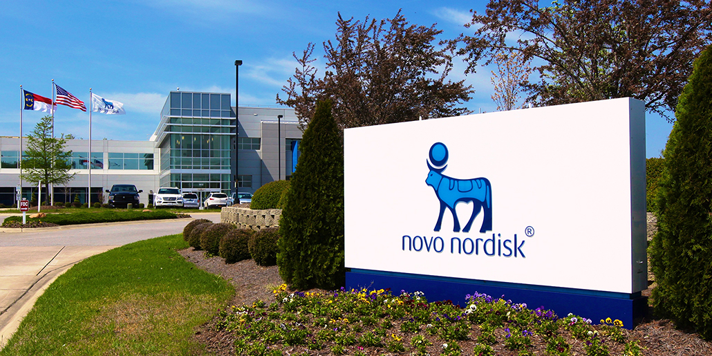 Front entrance of NovoNordisk facility. The company logo is on a white sign with the main building right behind it.