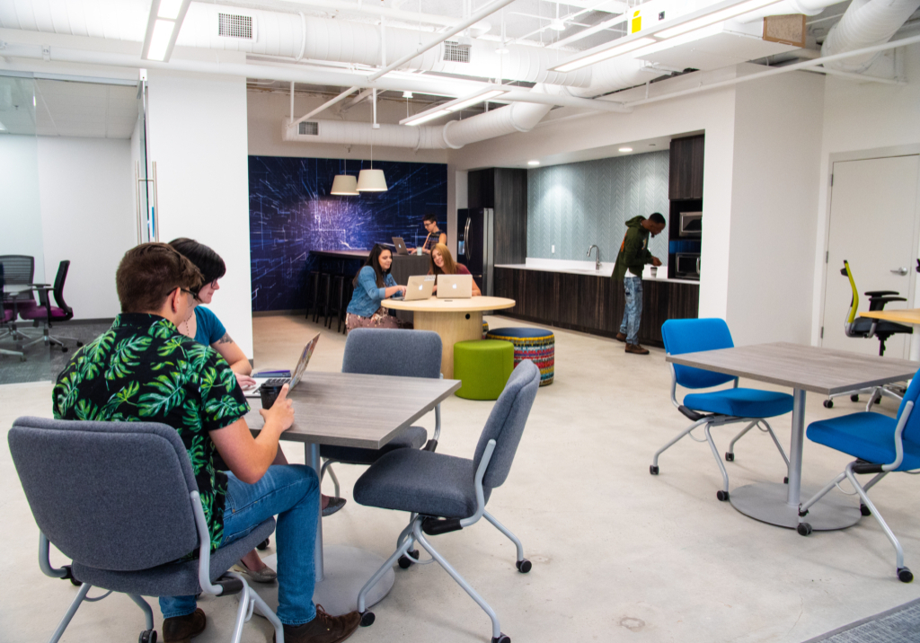 A workspace lit brightly by overhead LED lighting. There are various professionals working at tables.