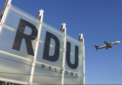 Front sign of RDU airport. An airplane is taking off in the background.