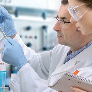 Two scientists wearing protective goggles and medical gloves. The two scientists closely examining lab results.