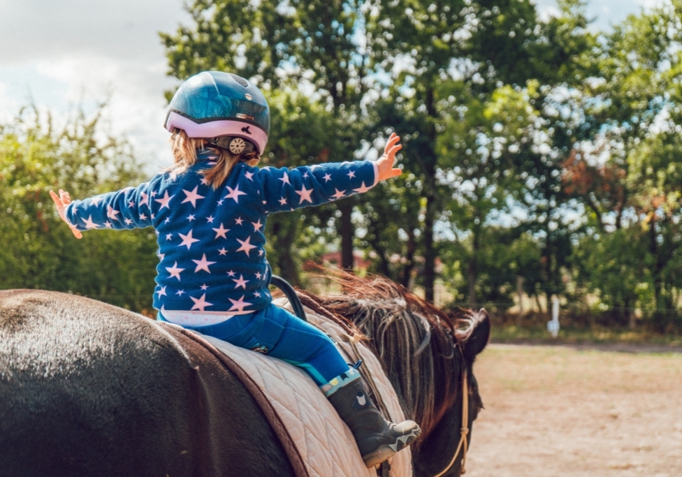 Young girl riding a horse and holding her hands out. The girl is wearing a distinctive blue outfit with moon and star patterns.