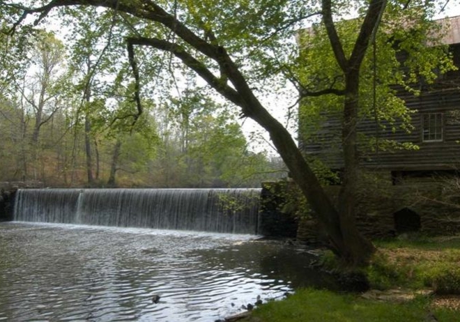 A water dam located in Warren County. Water is running over the dam into a calm pool below.